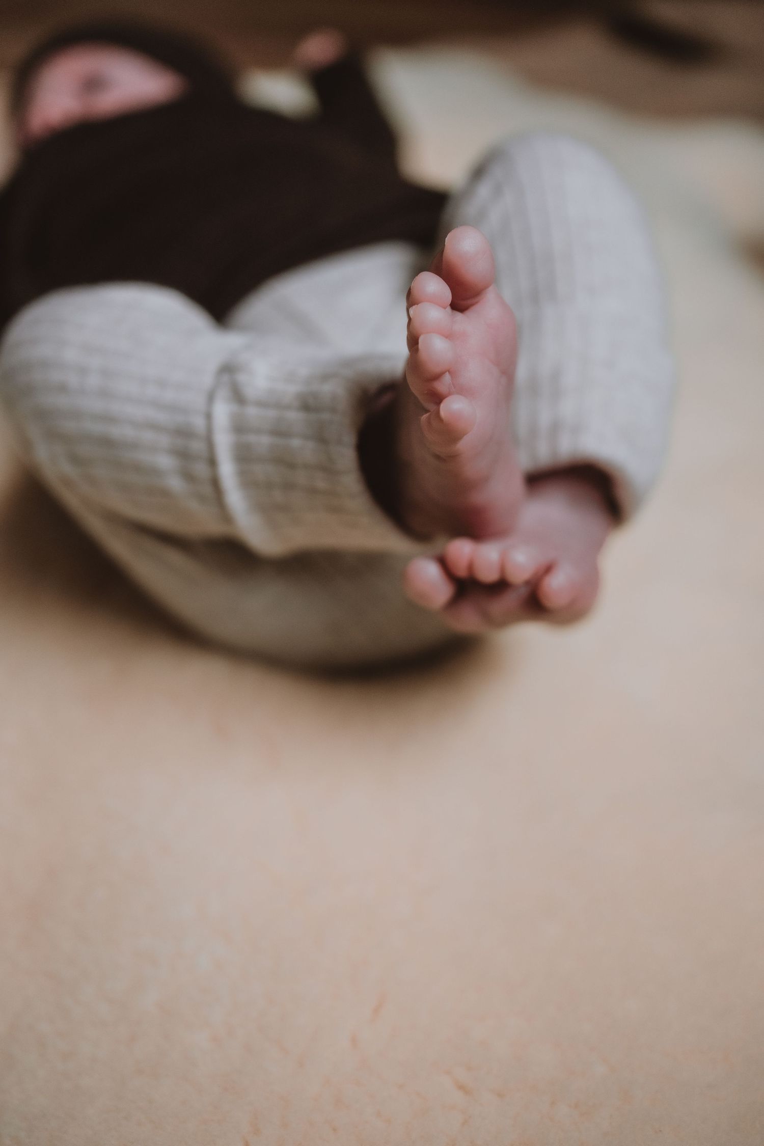 Close-up of tiny newborn baby feet in white knit pants lying on soft surface.