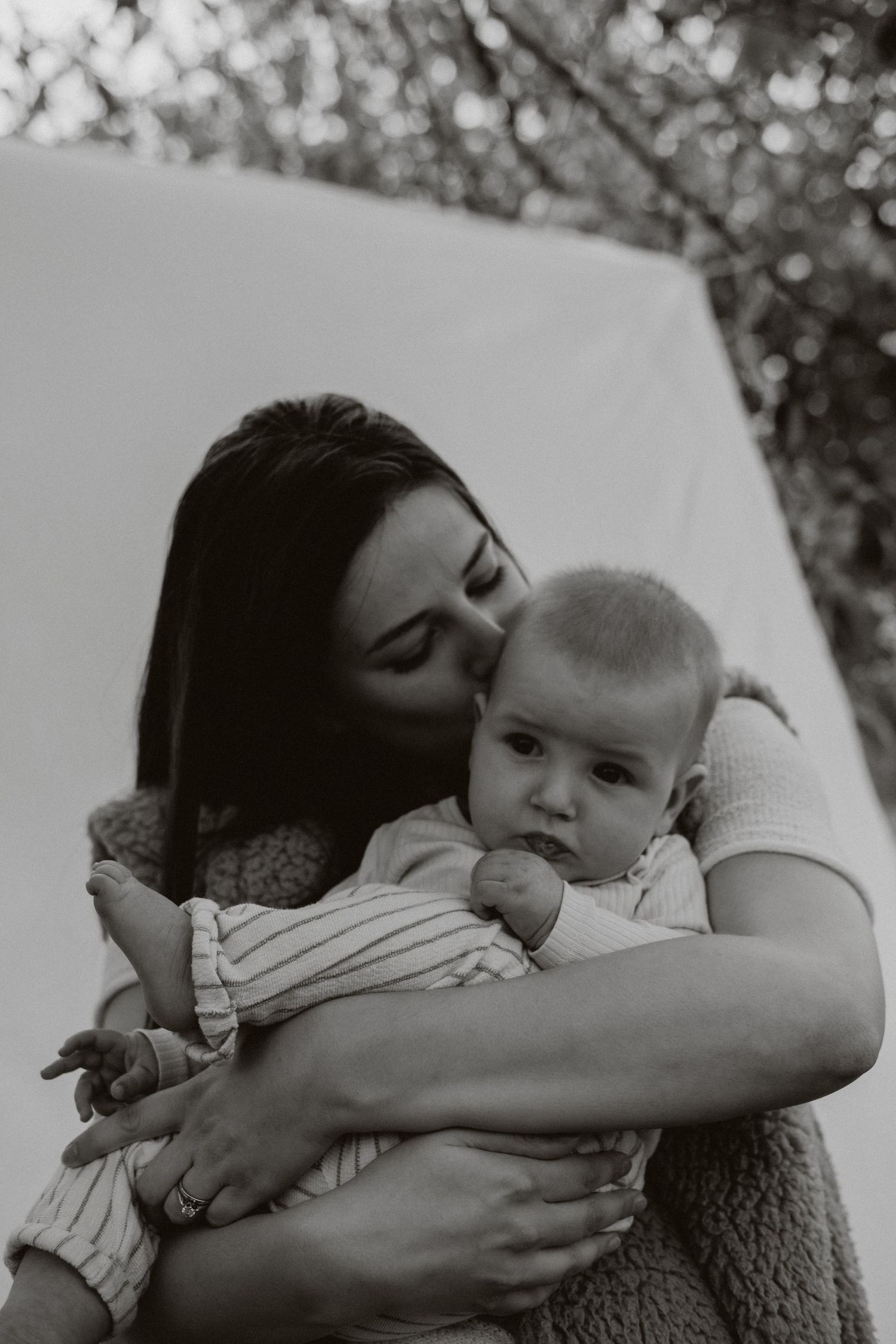 Loving mother kissing baby while holding them close in black and white photo.