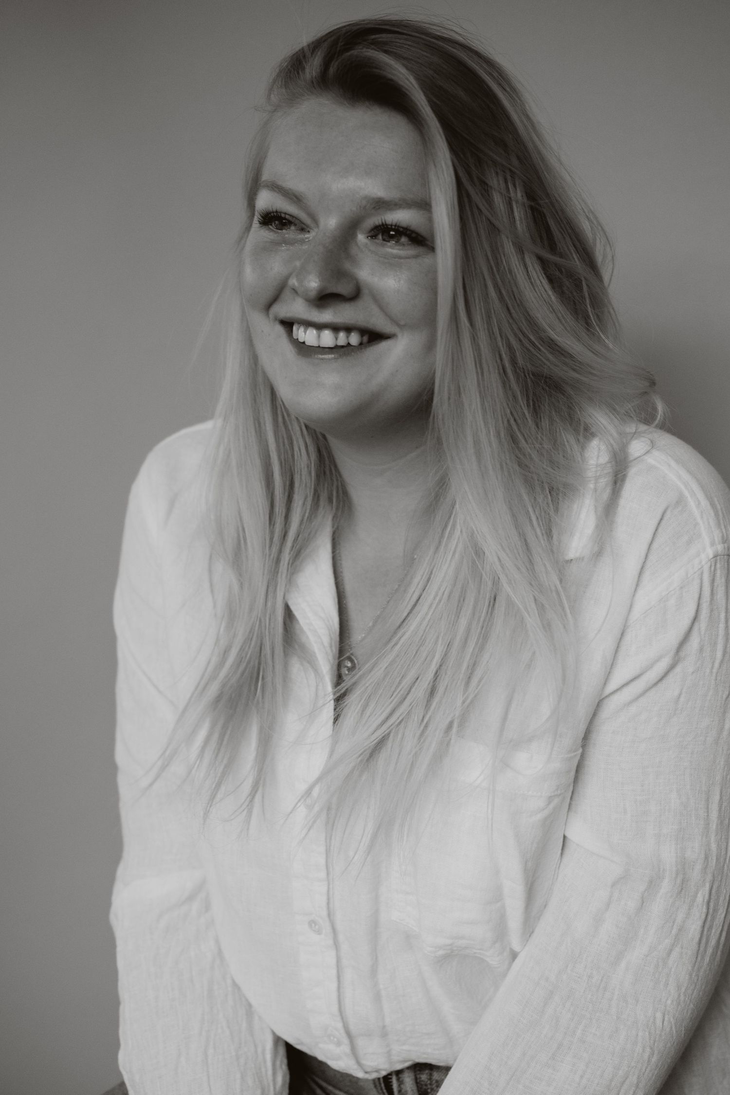 Smiling blonde woman in white shirt poses in black and white portrait photo.