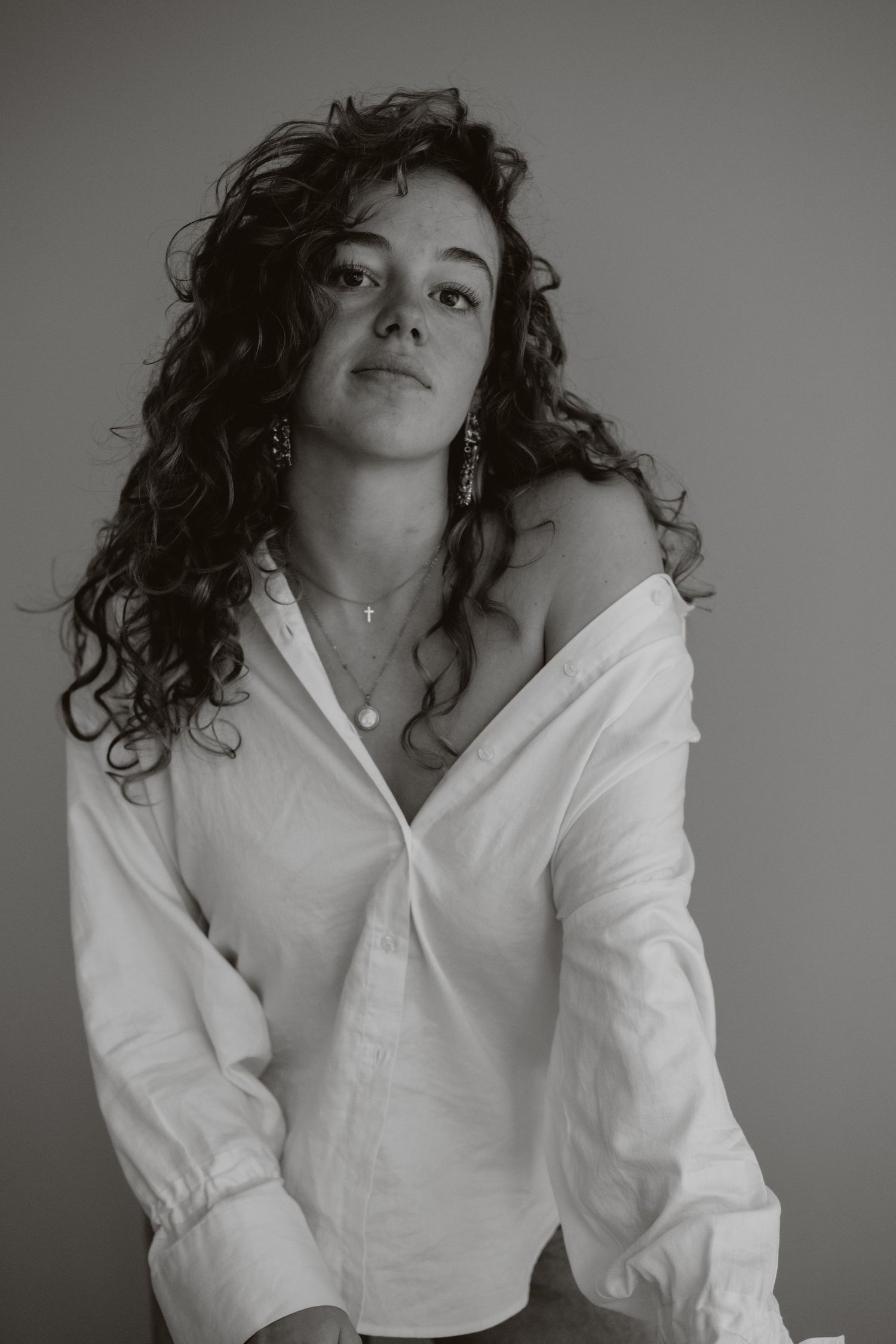 Black and white portrait of curly-haired woman in white off-shoulder shirt, studio photography.