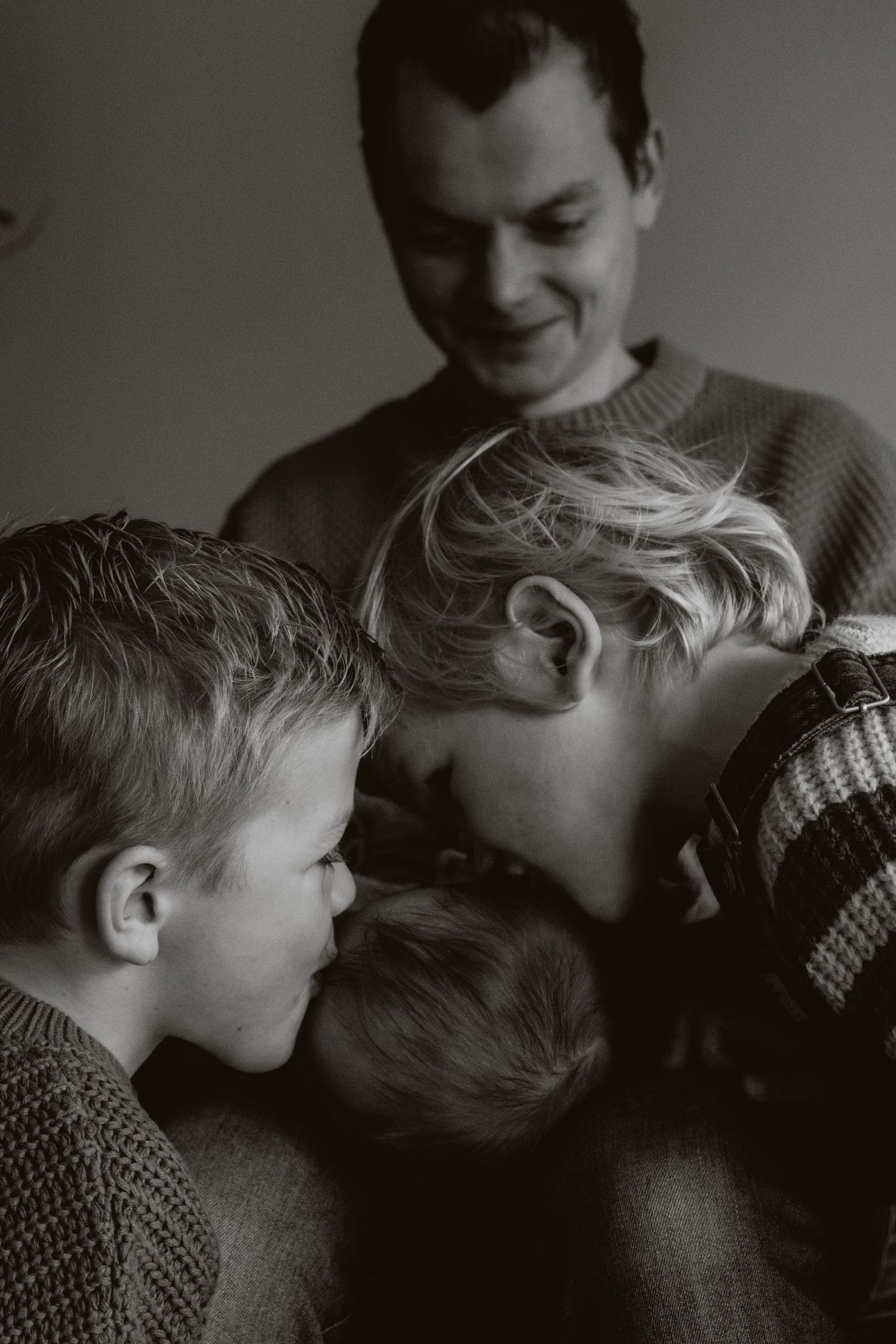 Father smiling warmly as children huddle together in black and white family photo.