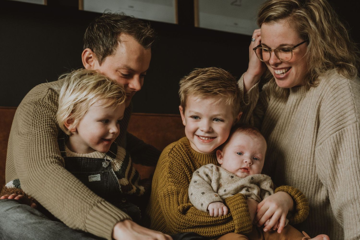 Happy family of five with newborn baby smiling together in warm cozy setting.
