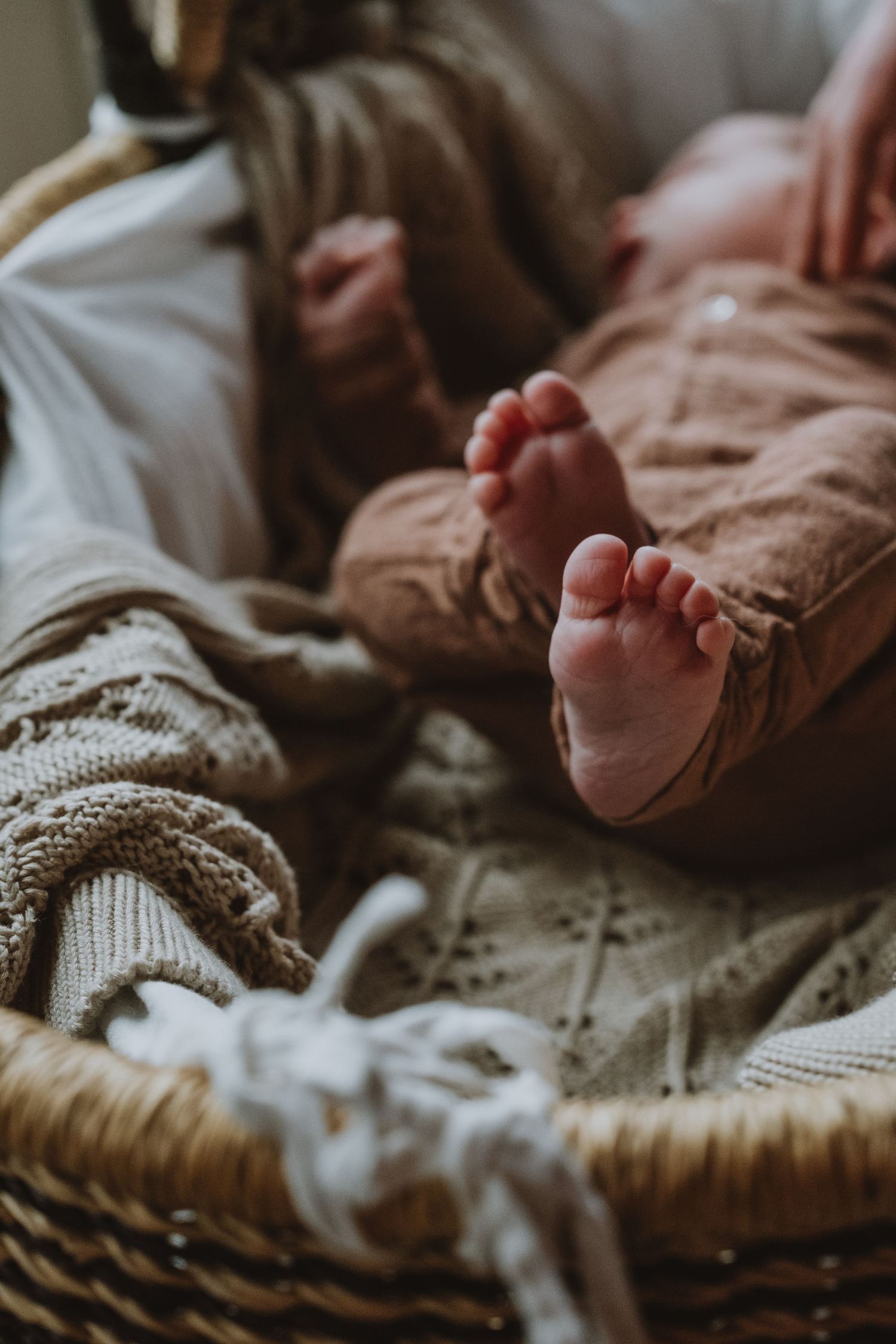Close-up of newborn baby feet in a rustic wicker basket with soft knit blankets.