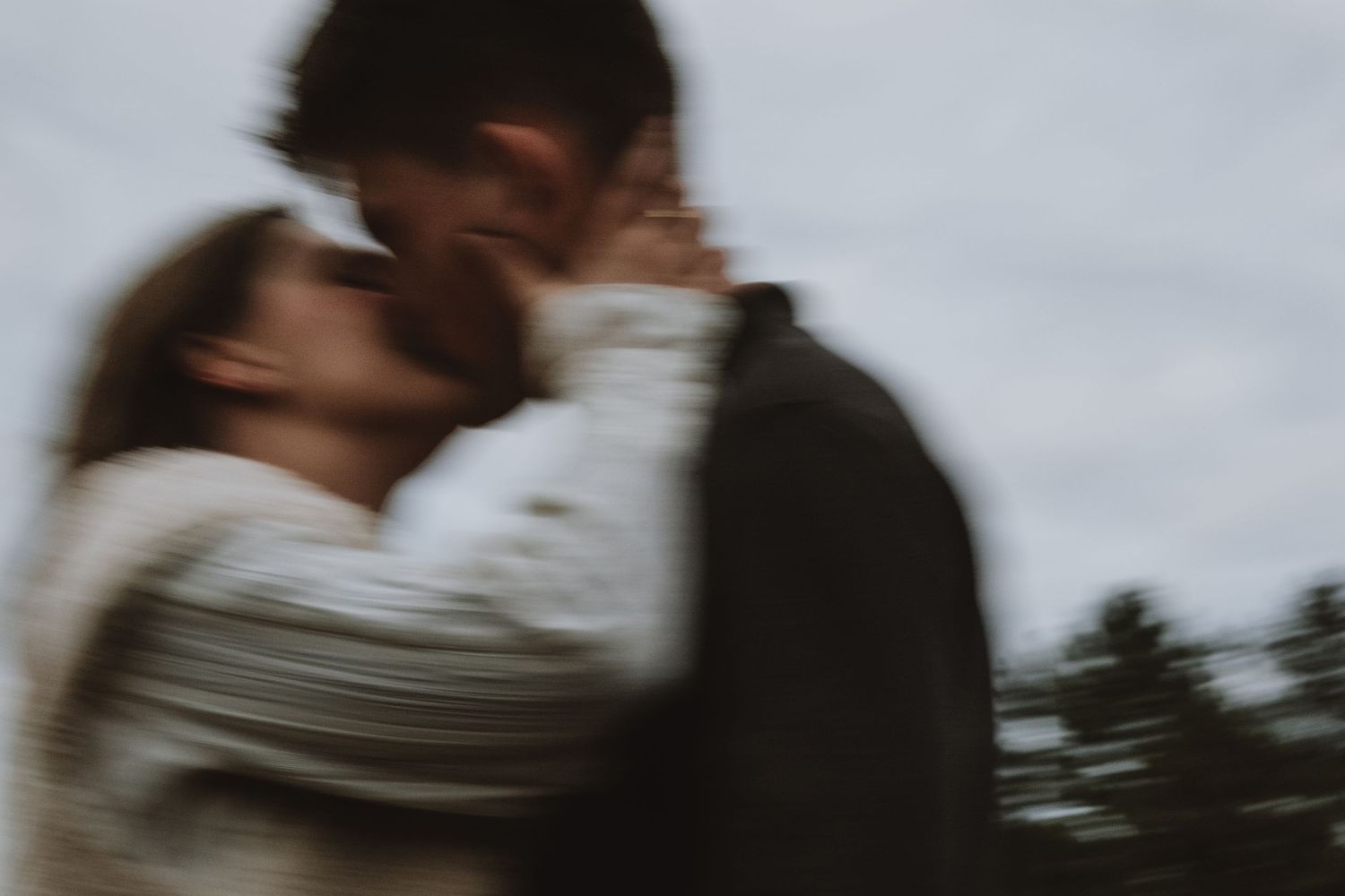Blurred romantic image of a couple sharing a kiss outdoors with trees in the background.