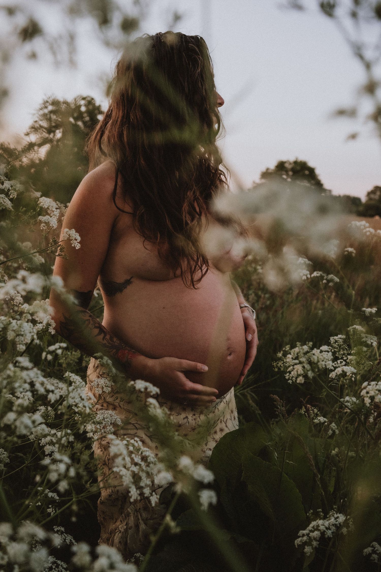 Zwangere vrouw met tattoos in avondzon tussen de bloemen