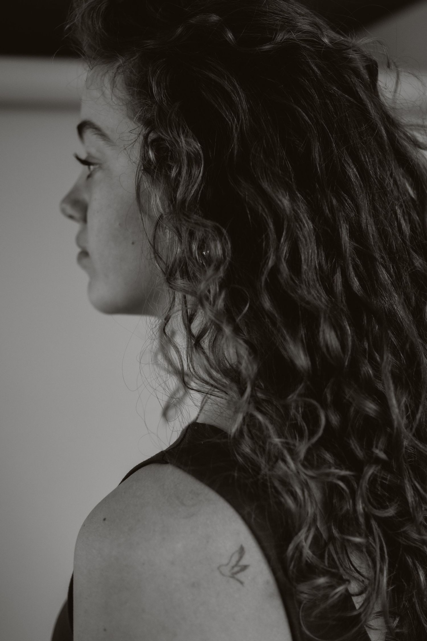 Black and white side profile of a woman with voluminous curly hair and a small shoulder tattoo.