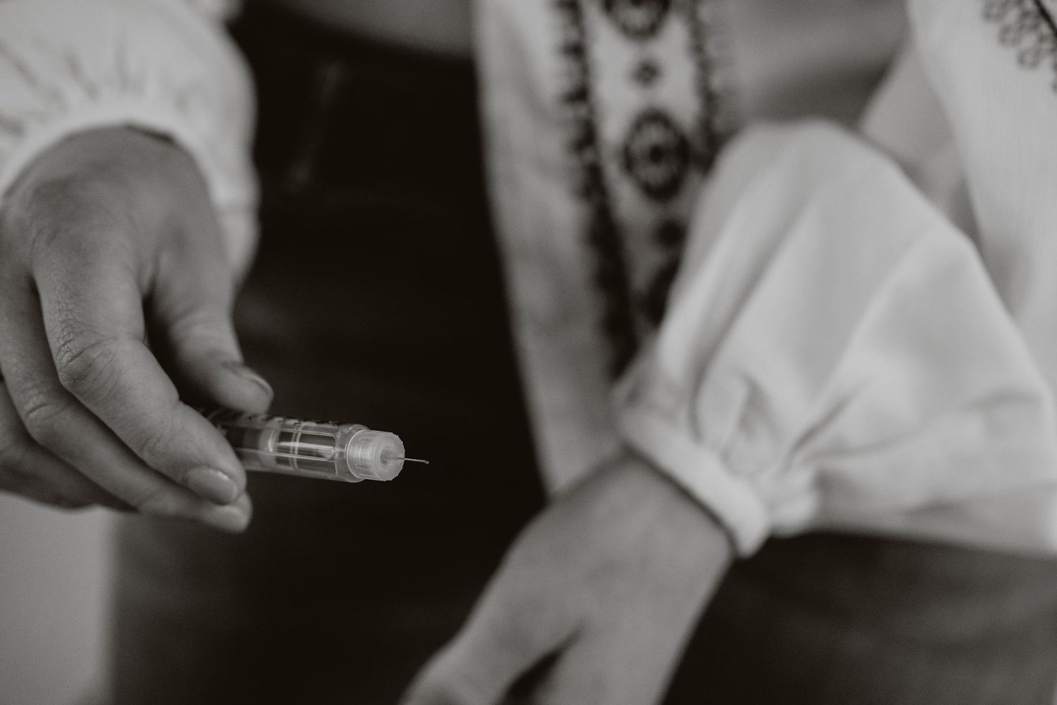 Black and white close-up of hands holding a small glass vial or capsule.