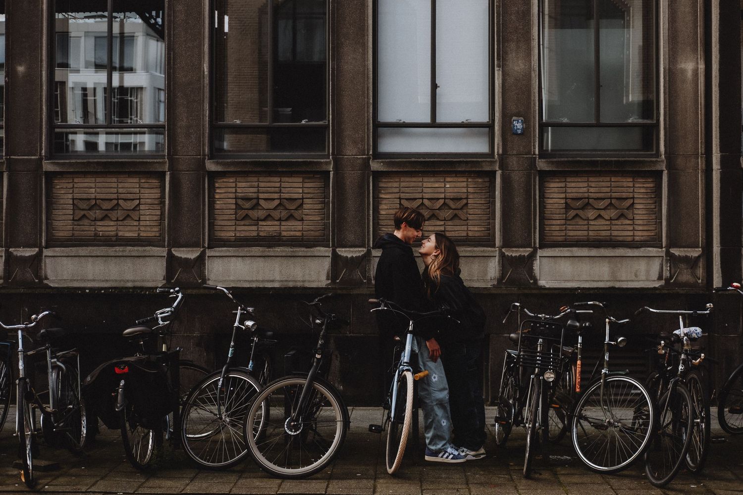 Romantic couple kissing between parked bicycles against a historic brick building facade.