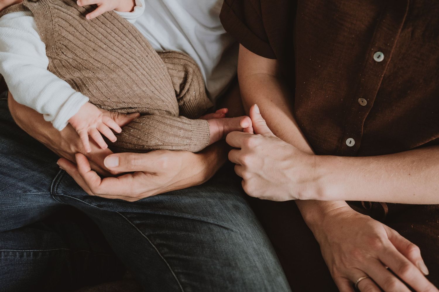 Close-up of parents hands gently holding newborn babys tiny feet and hands together.