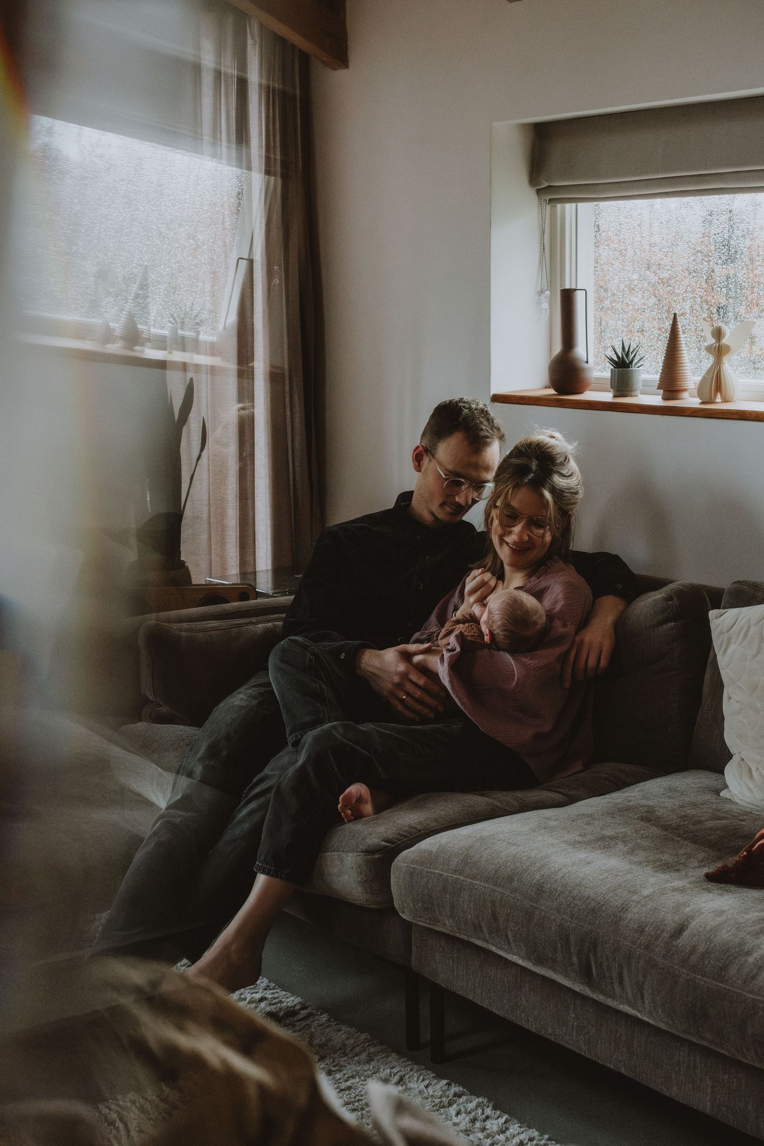 Young family sitting together on a cozy sofa holding their newborn baby at home.