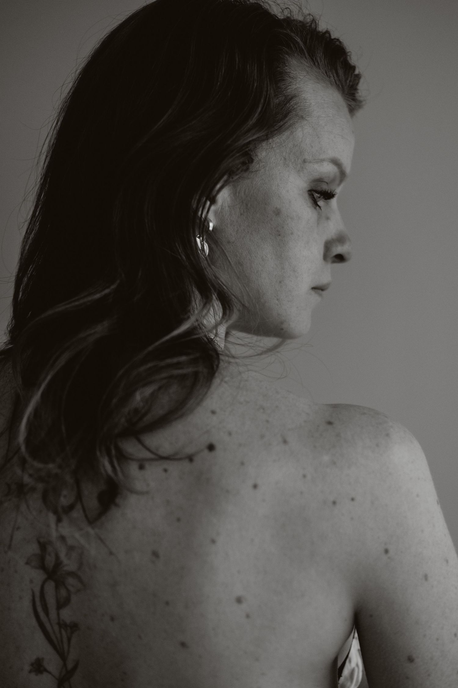 Black and white back portrait of a woman with freckles and a floral tattoo.