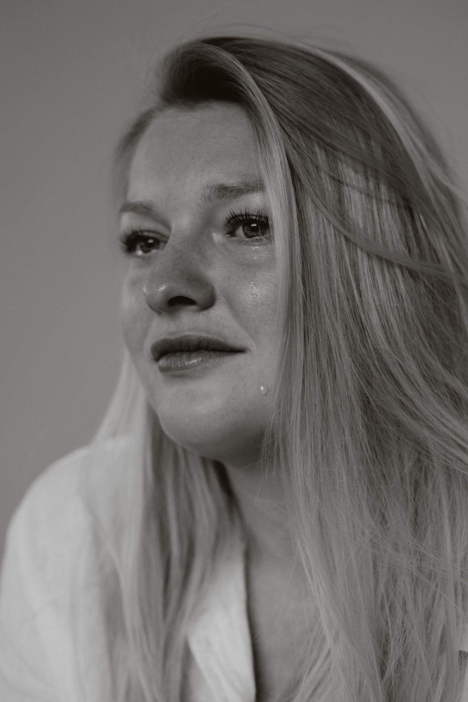 Emotional blonde woman with tears on cheeks in black and white close-up portrait.