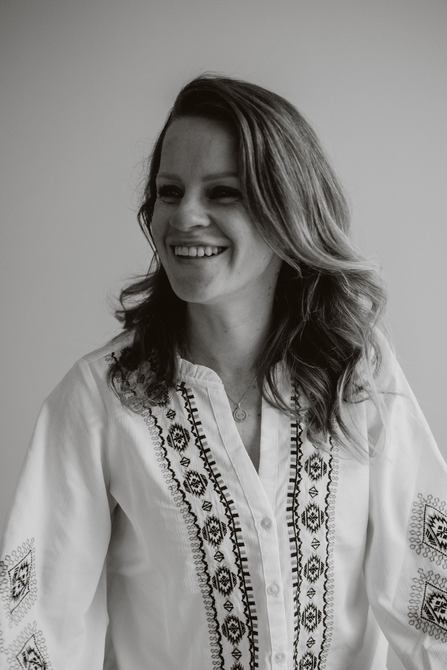 Smiling woman in embroidered white blouse photographed in black and white against a light background.