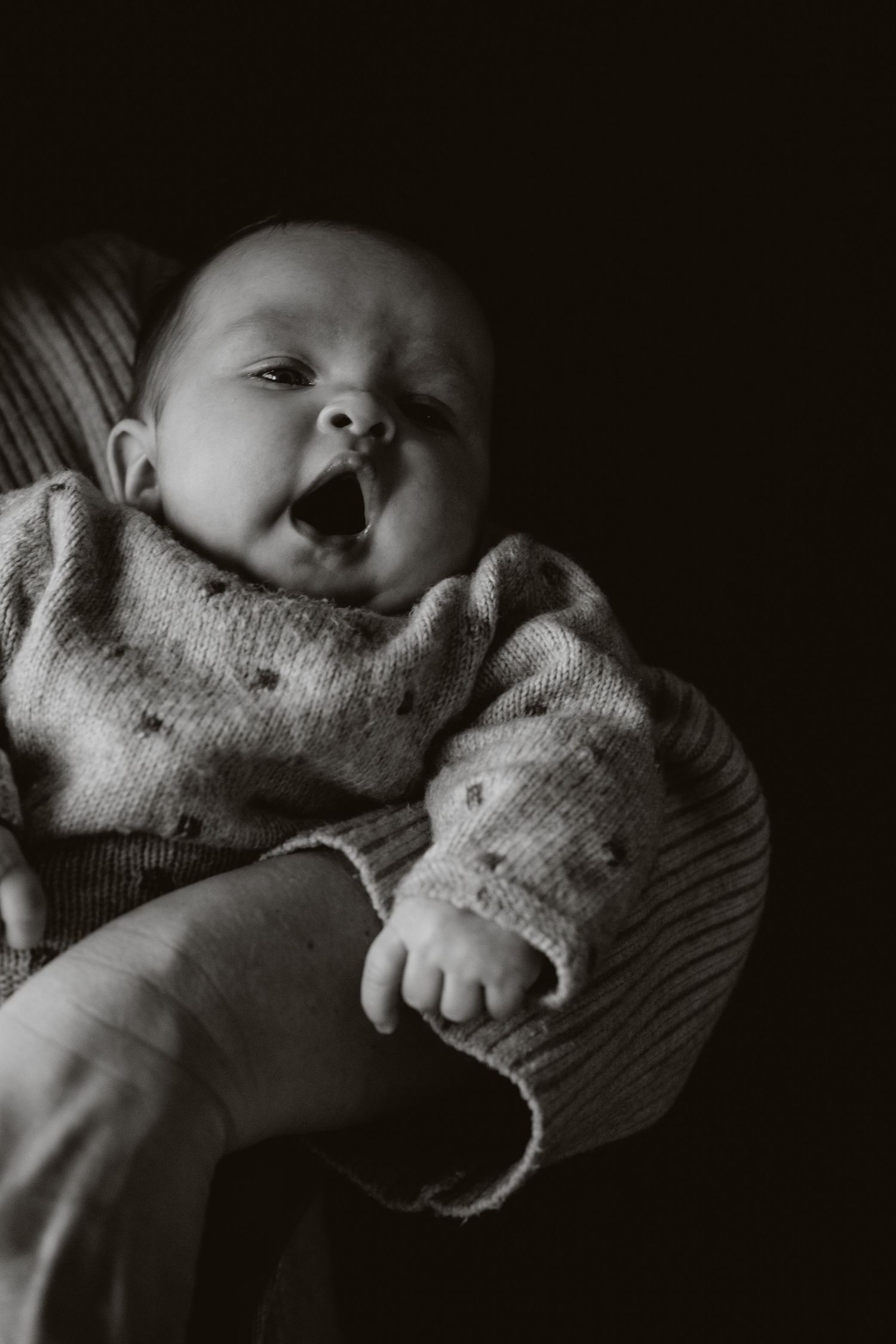 Adorable laughing newborn baby in cozy knit outfit captured in black and white.