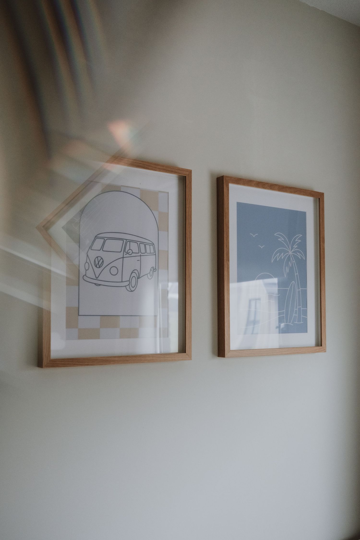 Two framed art prints featuring a VW bus and tropical palm tree hang on a neutral wall.