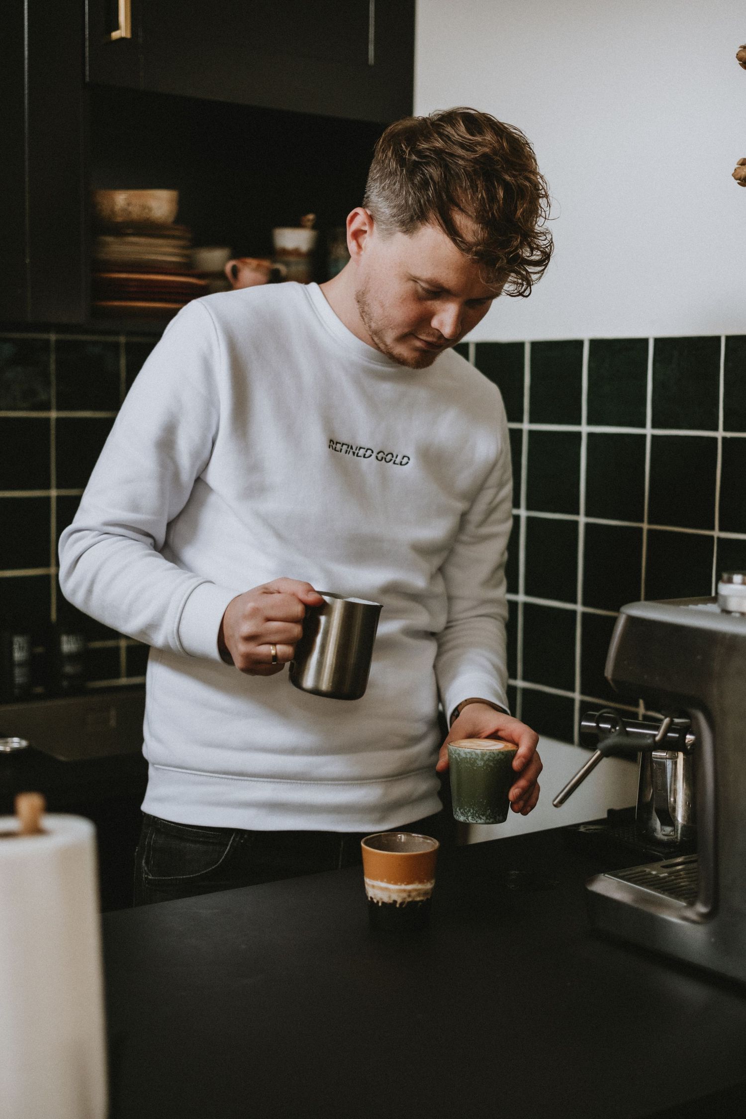Man in white sweatshirt preparing coffee at a modern kitchen espresso machine.