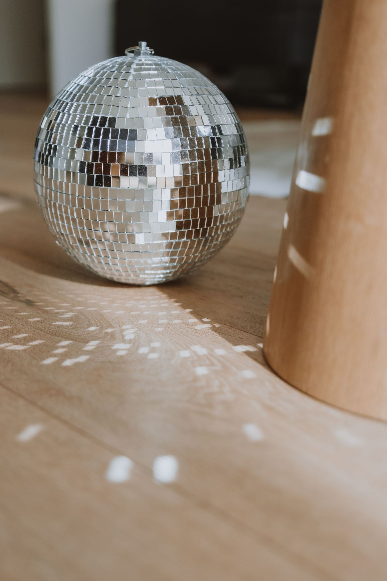 Shiny silver disco ball resting on wooden floor beside a cylindrical wooden object indoors.