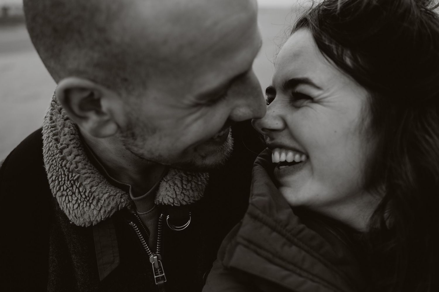 Black and white photo of a laughing couple sharing an intimate moment outdoors.