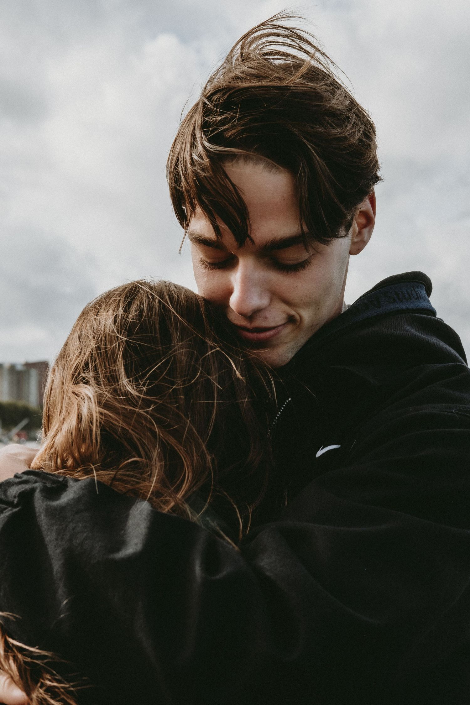 Young couple embracing tenderly outdoors under a cloudy sky.