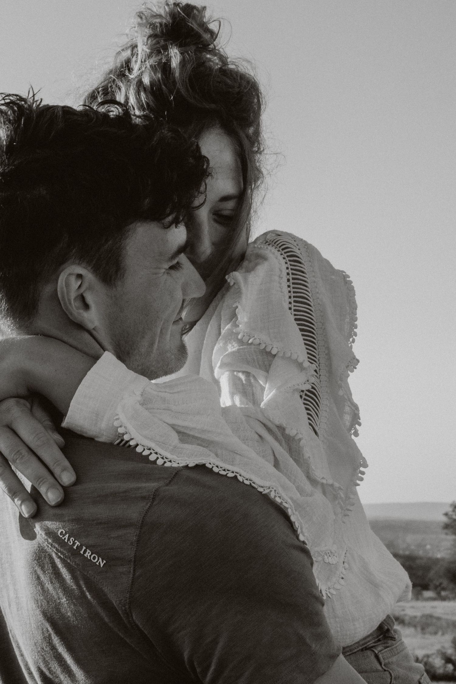 Black and white photo of a joyful couple embracing and smiling against an open sky backdrop.