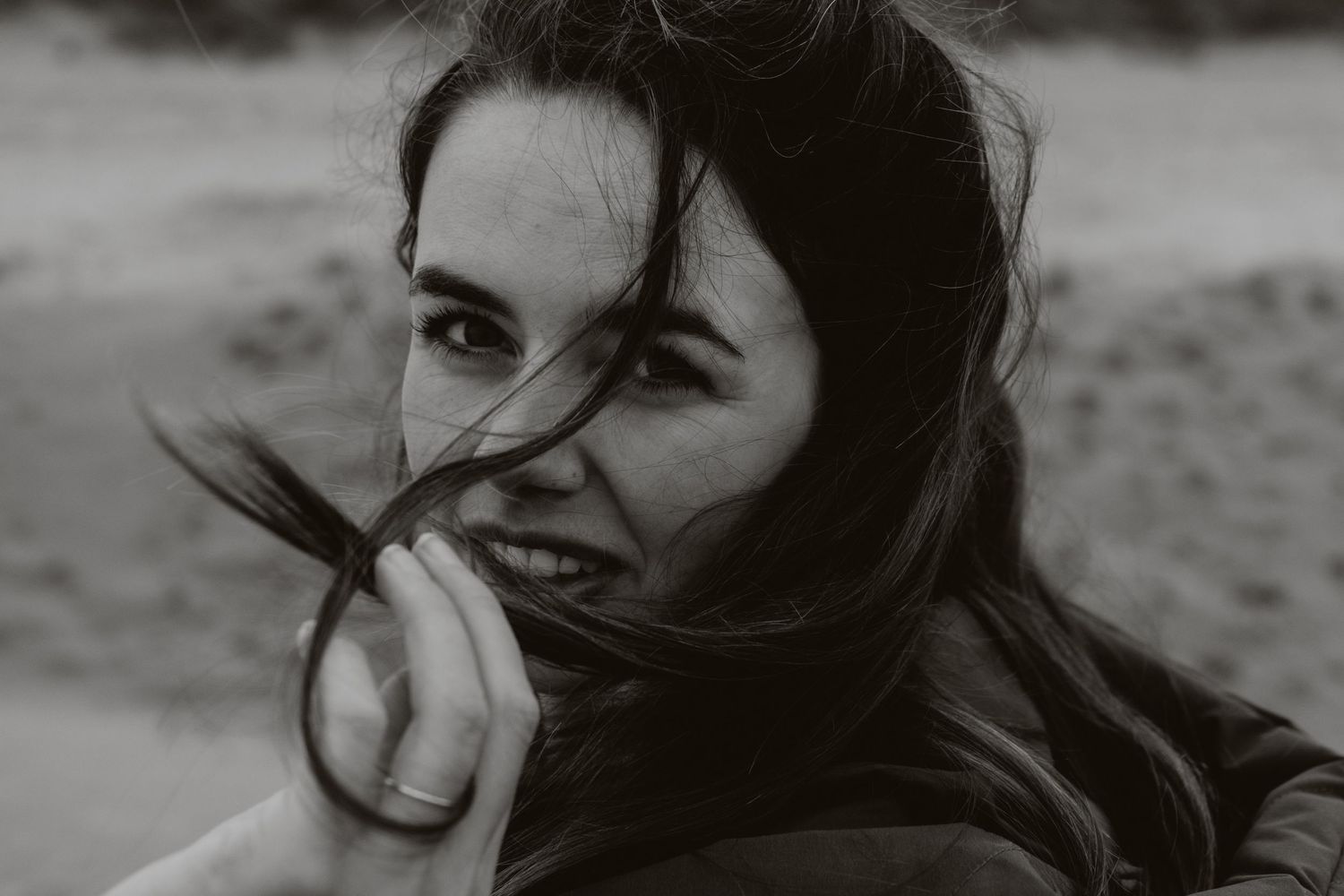 Black and white portrait of woman with wind-blown hair, candid outdoor photography.
