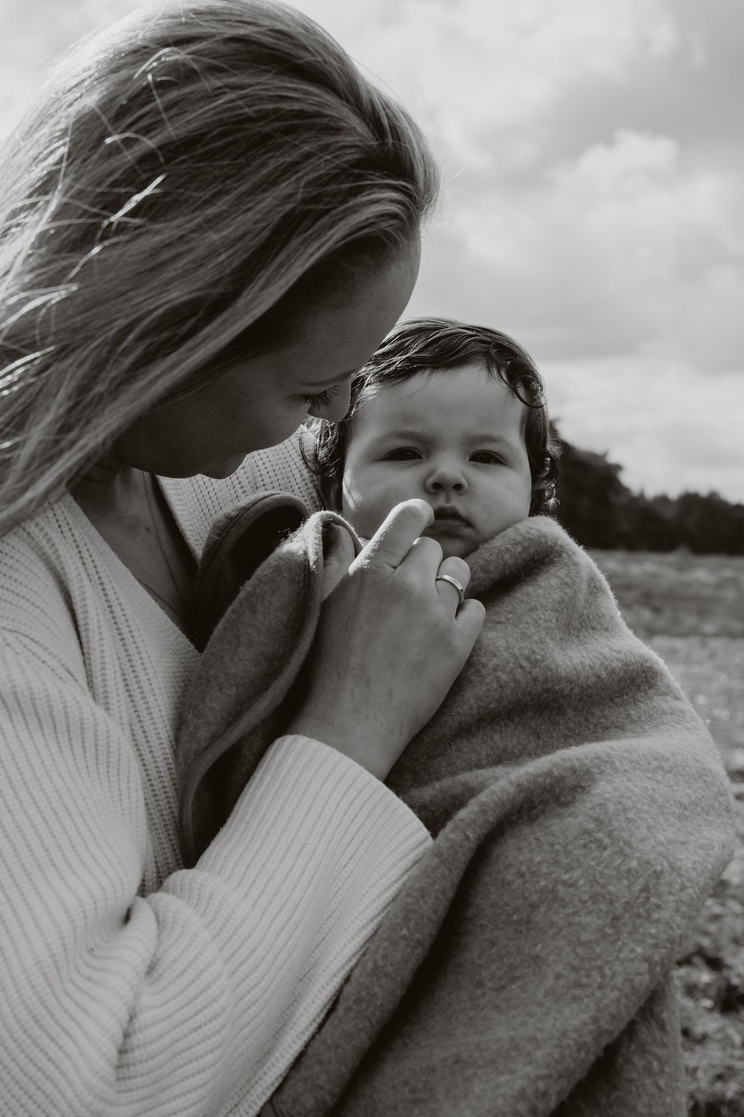 Black and white photo of mother tenderly holding baby wrapped in blanket.