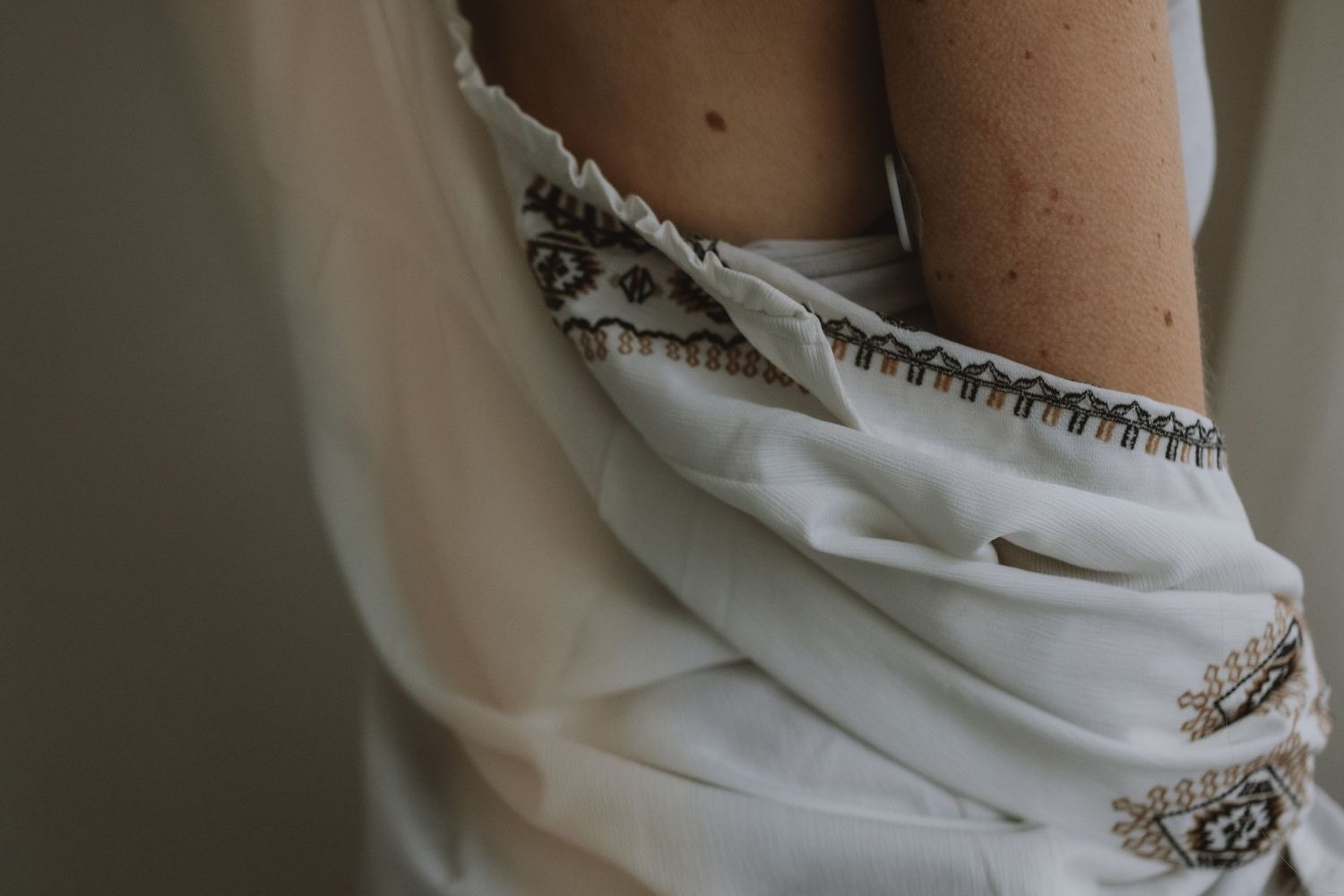 Close-up detail of embroidered white dress fabric with beaded trim at waist.