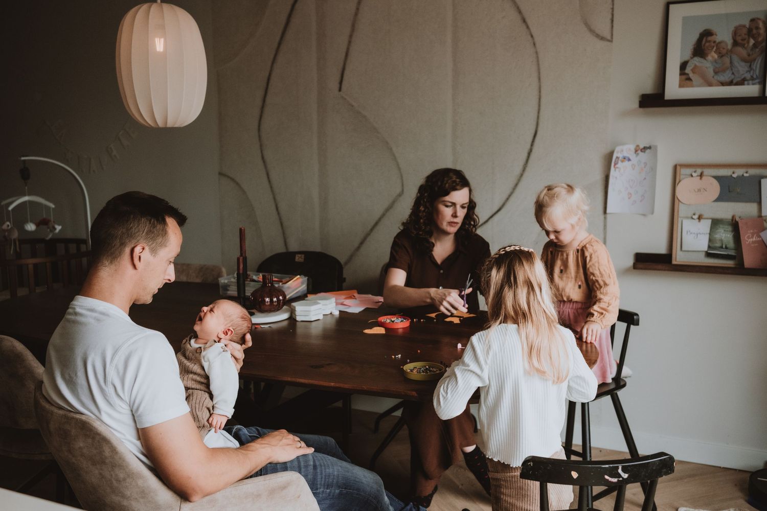 Een gezellige gezinstafereel aan tafel, kinderen spelen, baby slaapt.