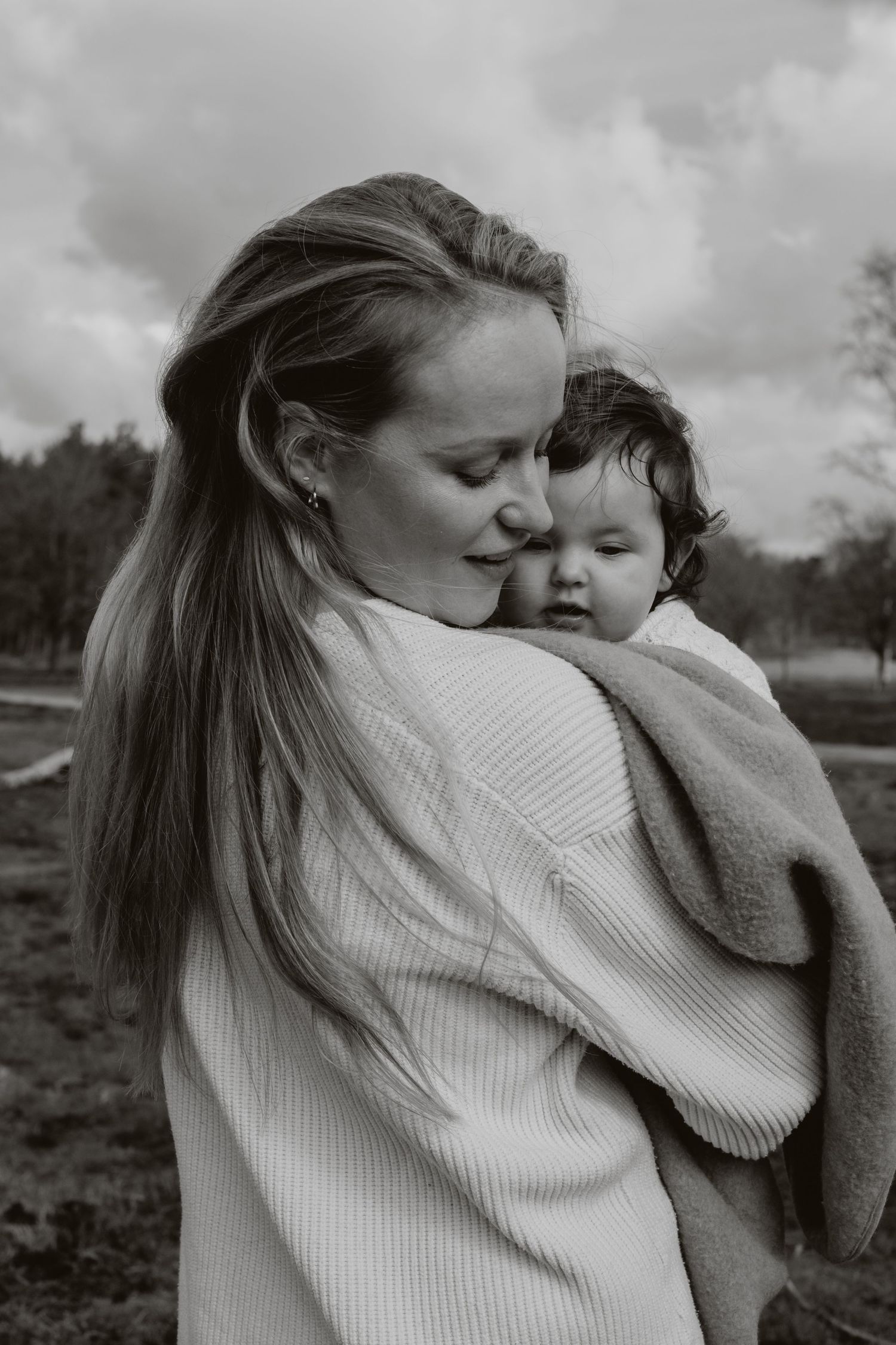 Black and white photo of a mother tenderly holding and nuzzling her baby outdoors.