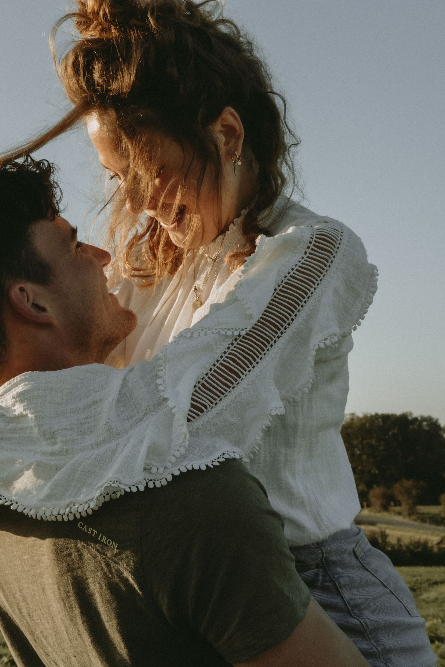 Man lifting woman in white blouse outdoors during golden hour in a joyful embrace.