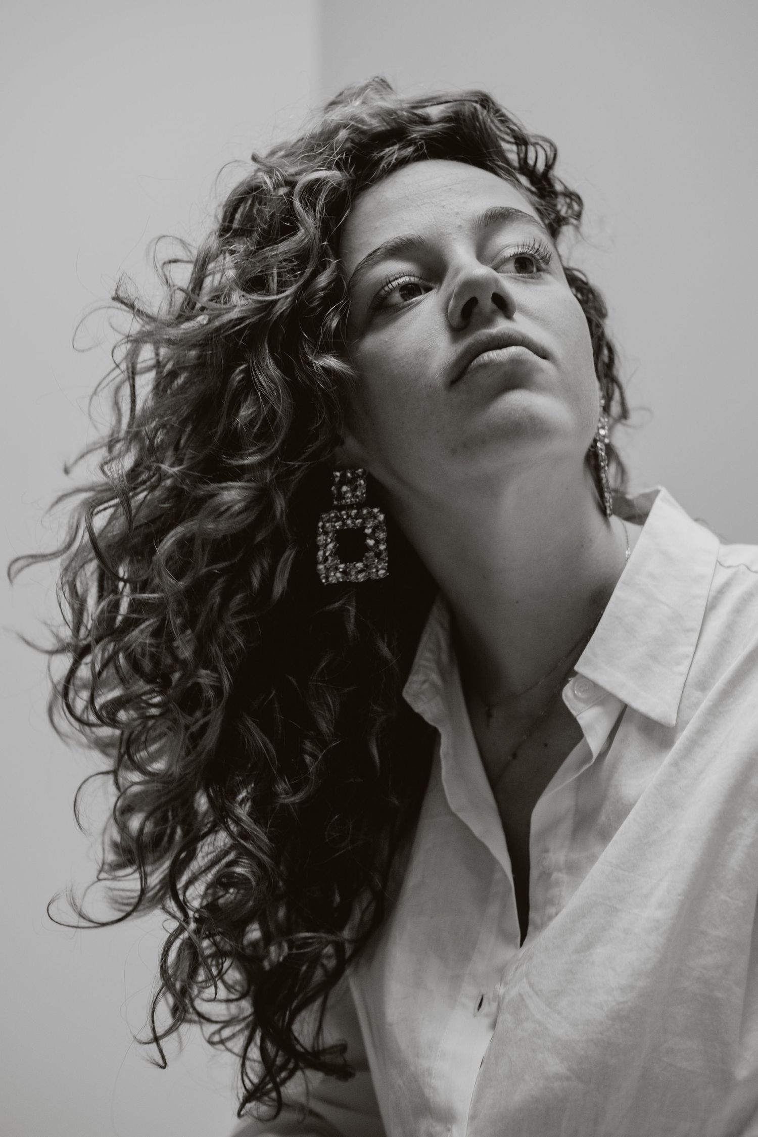 Black and white portrait of a curly-haired woman wearing statement square earrings and a white shirt.