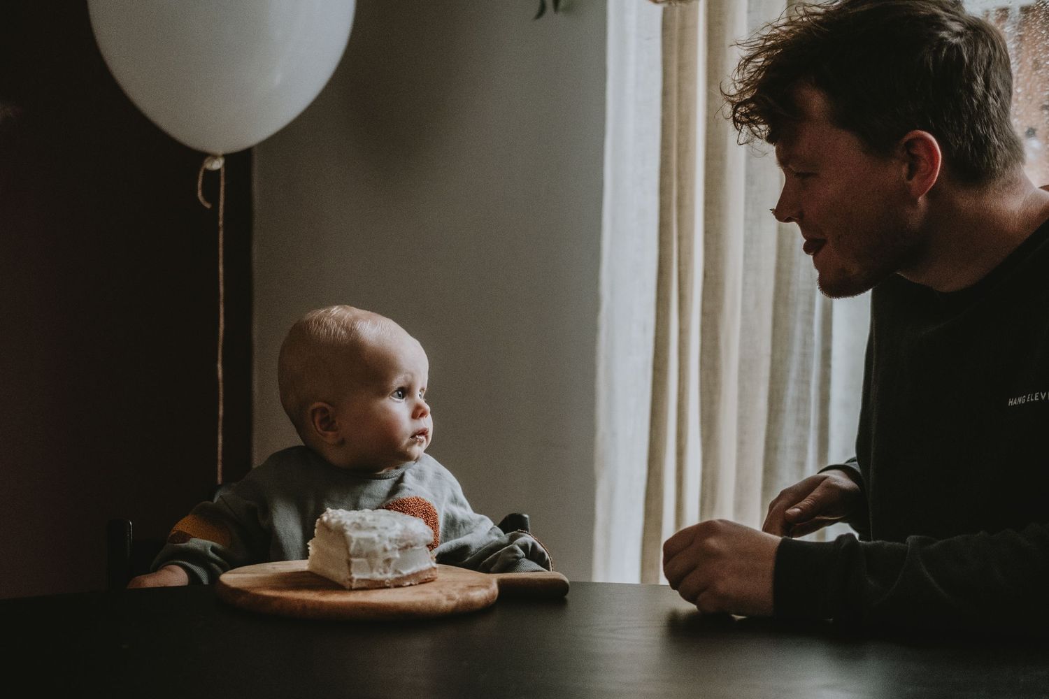 Father and baby sharing a tender moment at a table with a birthday cake and balloon.