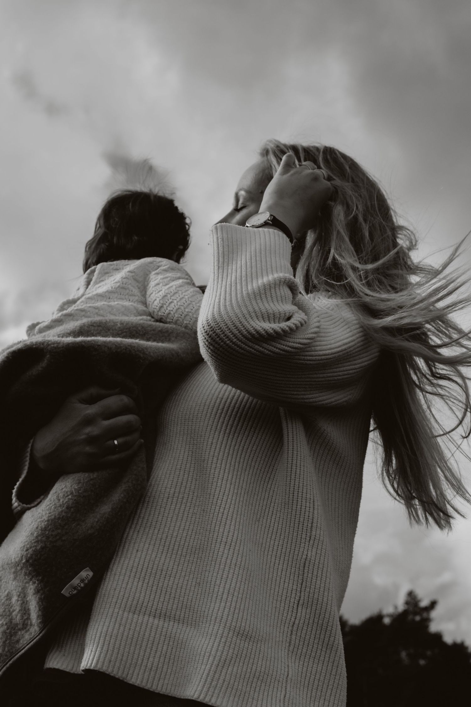 Low angle black and white photo of mother carrying child under dramatic cloudy sky.