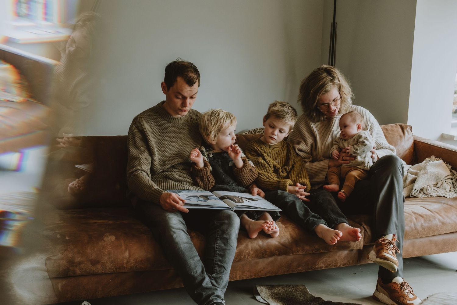 Happy family of five reading a book together on a couch at home.