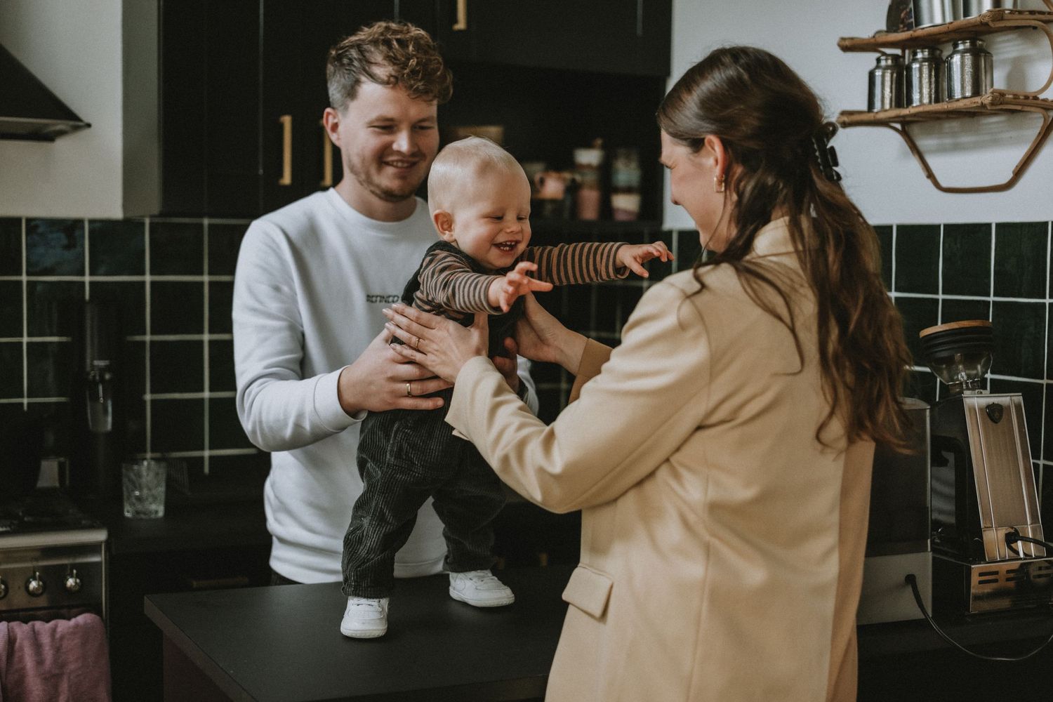 Happy young family with father holding baby while mother interacts in a modern kitchen.