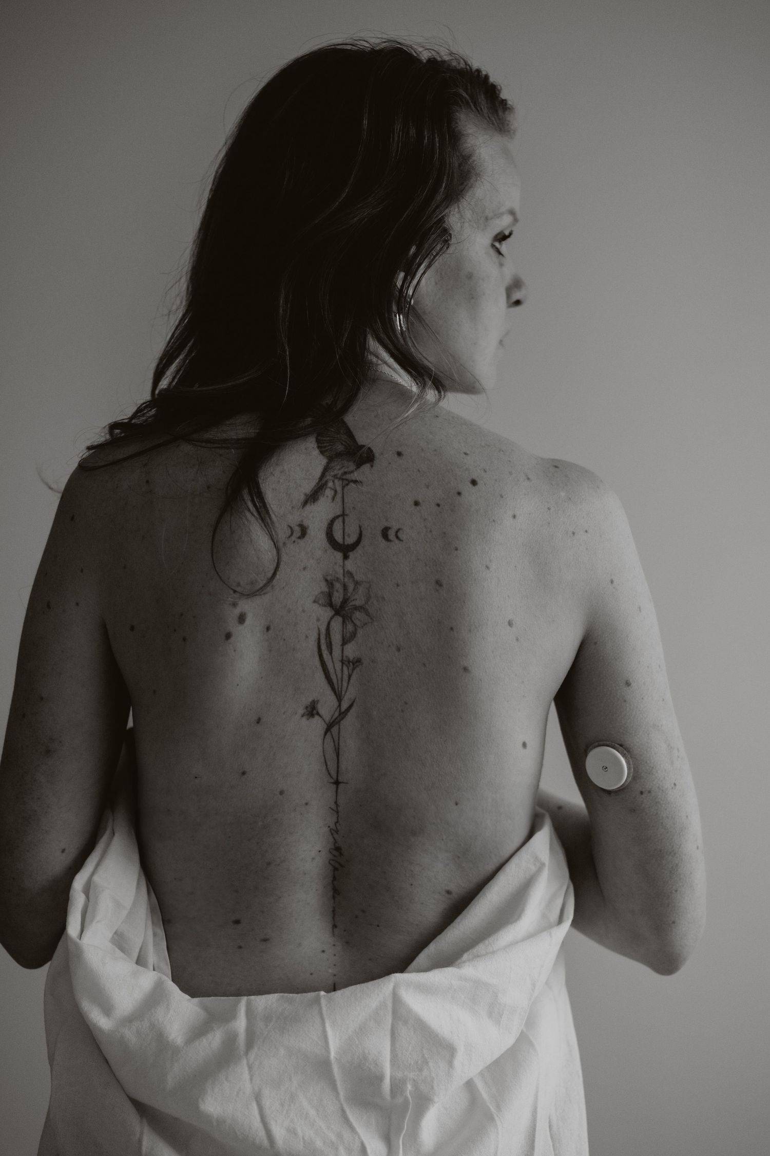 Woman with spine tattoo of floral design holding white towel, black and white photo.