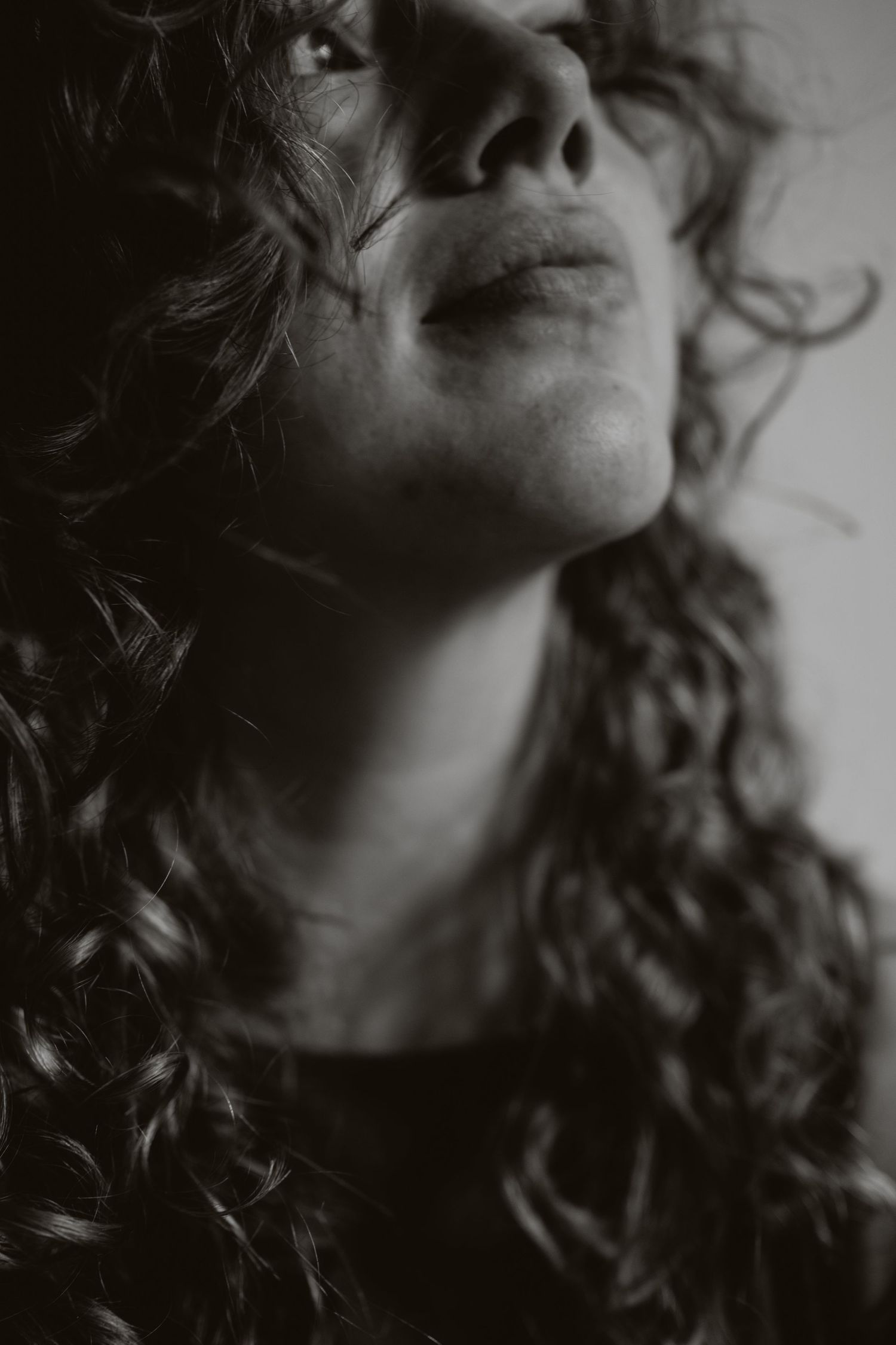 Dramatic black and white close-up portrait of curly-haired woman looking upward.