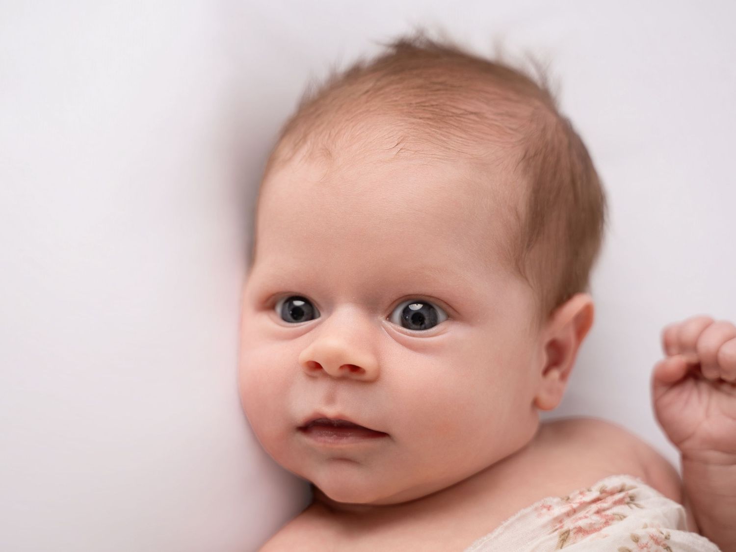 Close-up portrait of a newborn baby with blue eyes lying on a white surface.