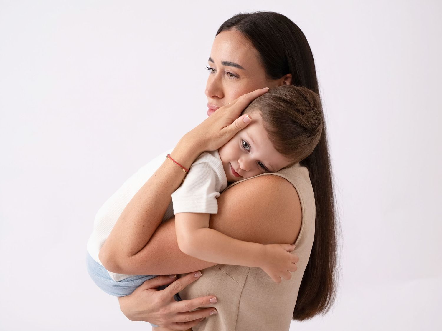 A mother with long dark hair tenderly holds her young child who rests their head on her shoulder.