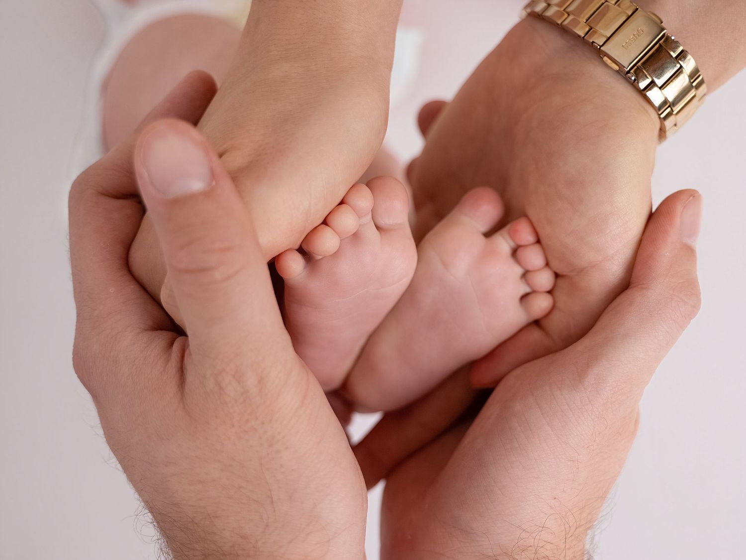 Adult hands gently cradling tiny newborn baby feet, symbolizing love and parental care.