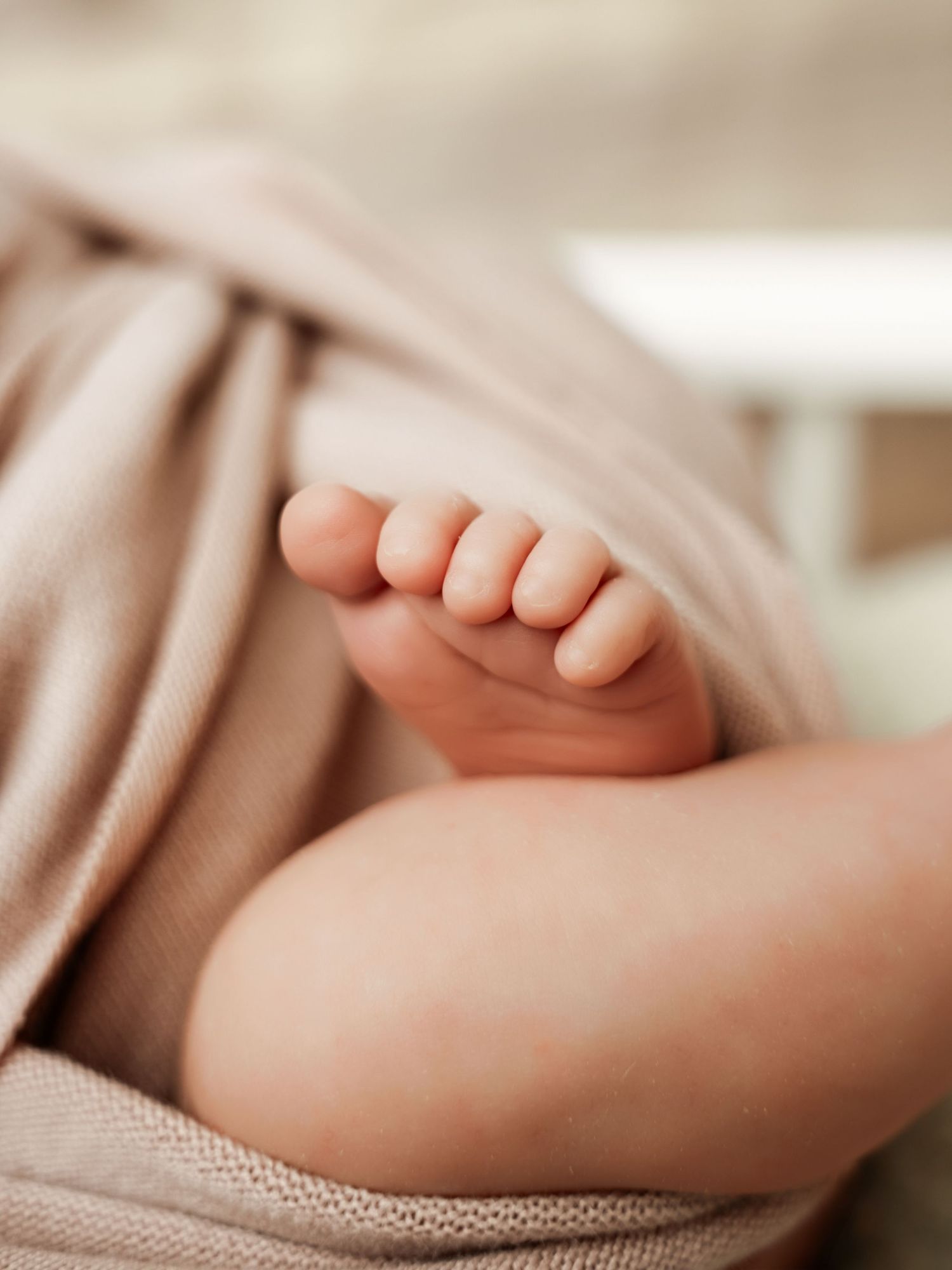 Close-up of a newborn baby's tiny foot peeking out from a soft pink knit blanket.