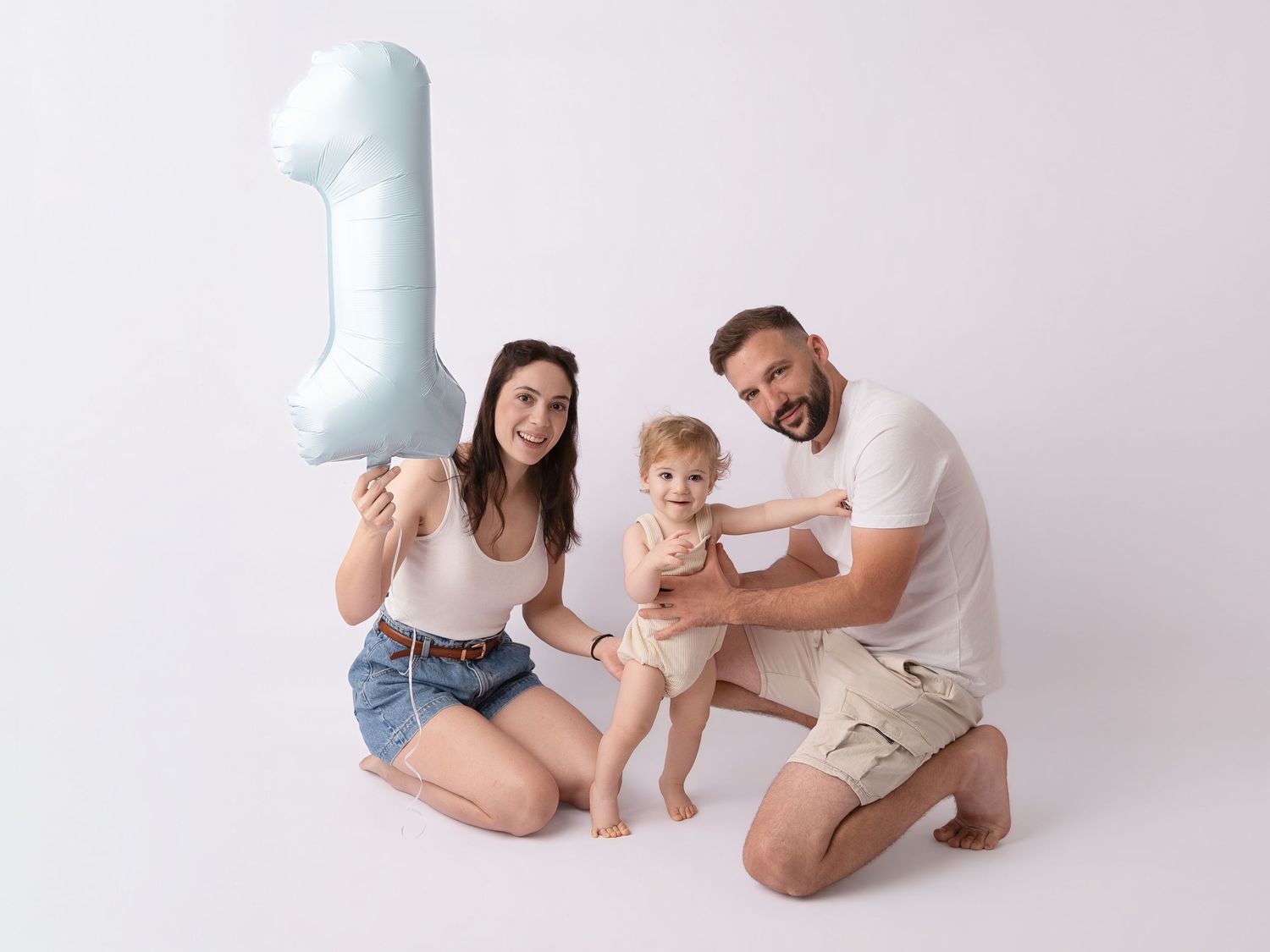 Family celebrating baby's first birthday with a number one balloon on white background.