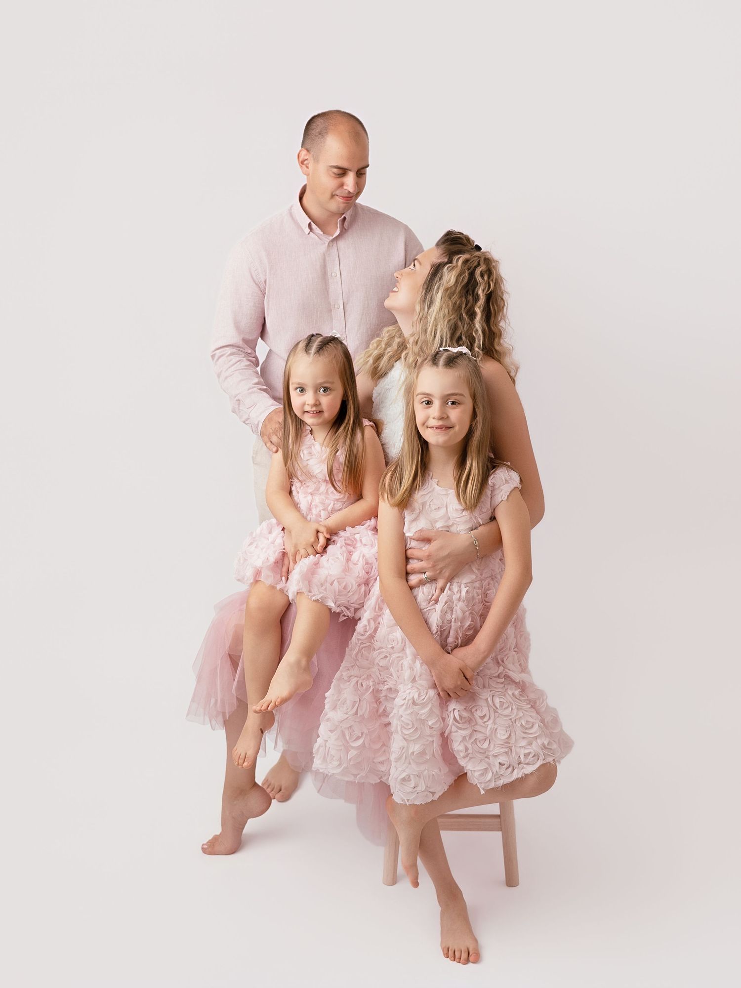 Family of four in matching pink outfits posing together in a bright studio portrait session.