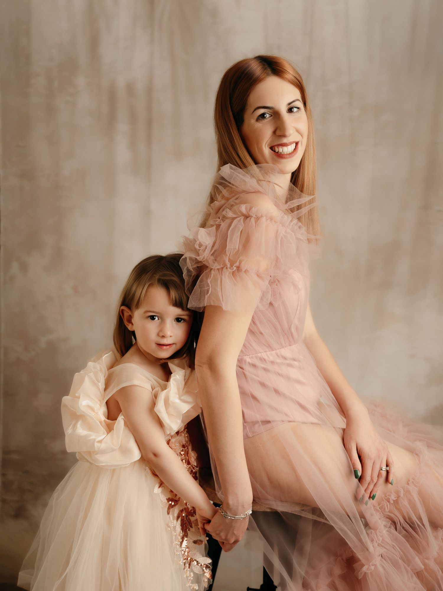 A mother and daughter pose together in matching pink and cream tulle dresses during an elegant studio photo session.