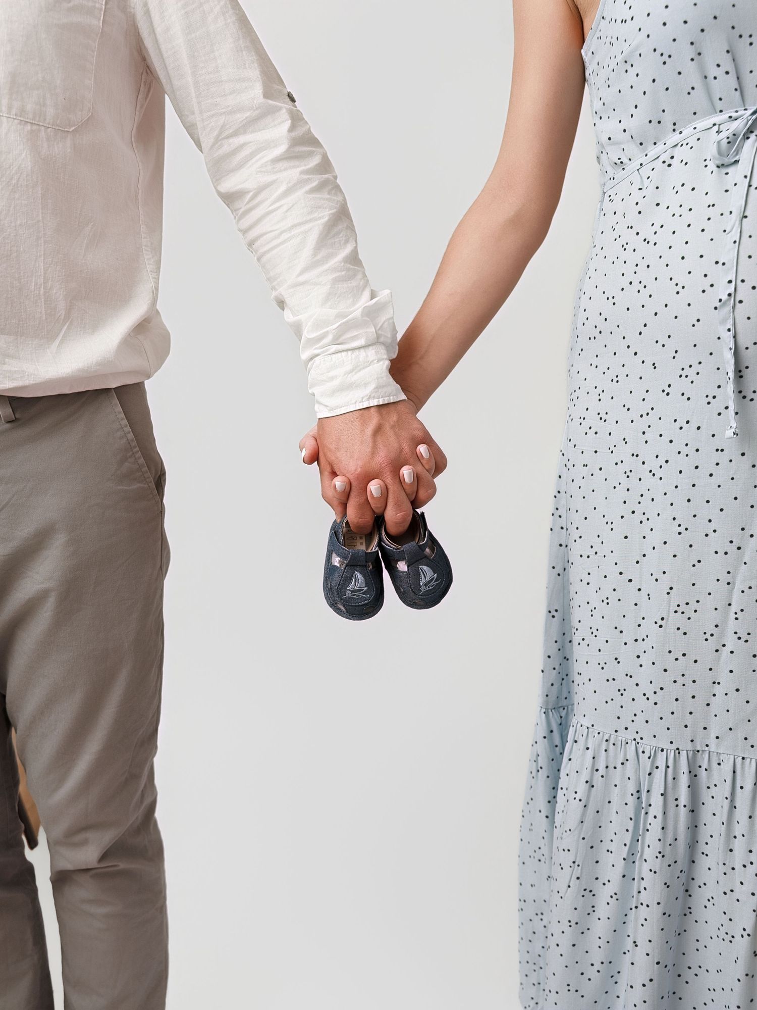 Couple holding hands and tiny baby shoes together during pregnancy announcement photo shoot.