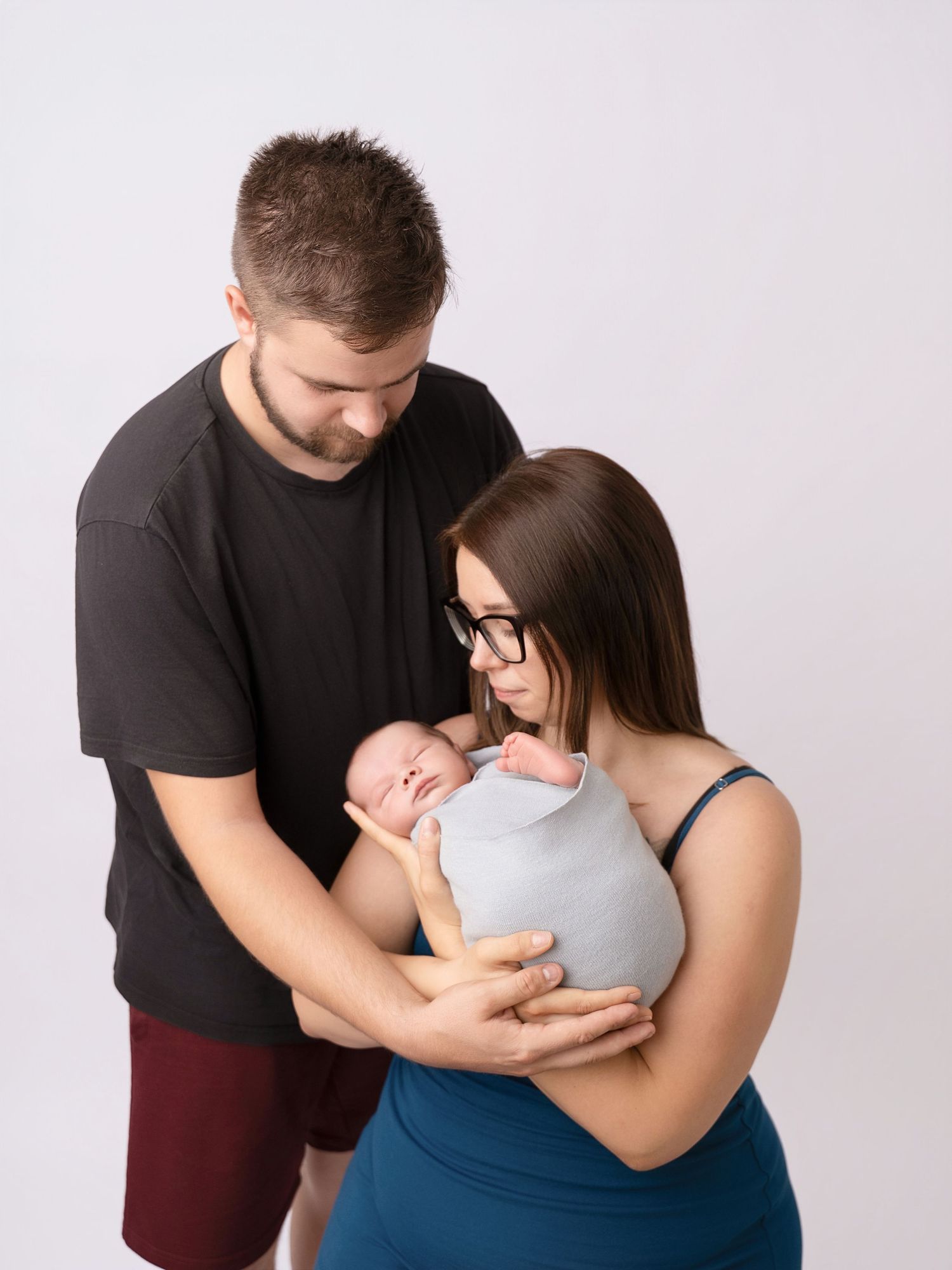 Young parents lovingly gaze at their swaddled newborn baby during a professional studio portrait session.