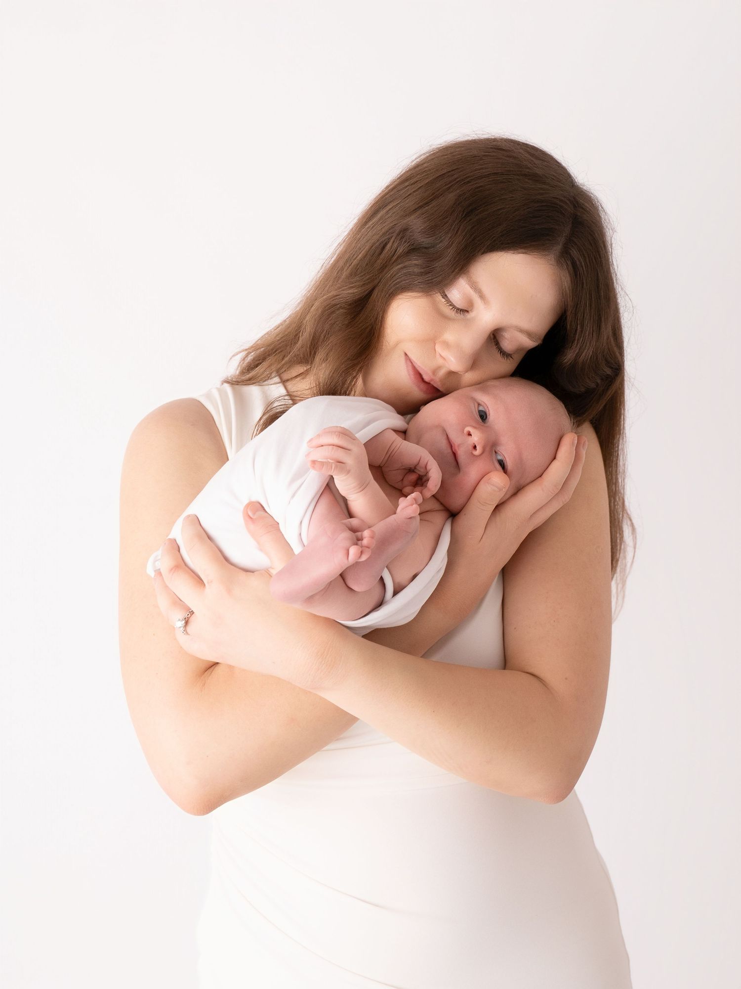 A mother tenderly holds her newborn baby close to her chest against a white background.