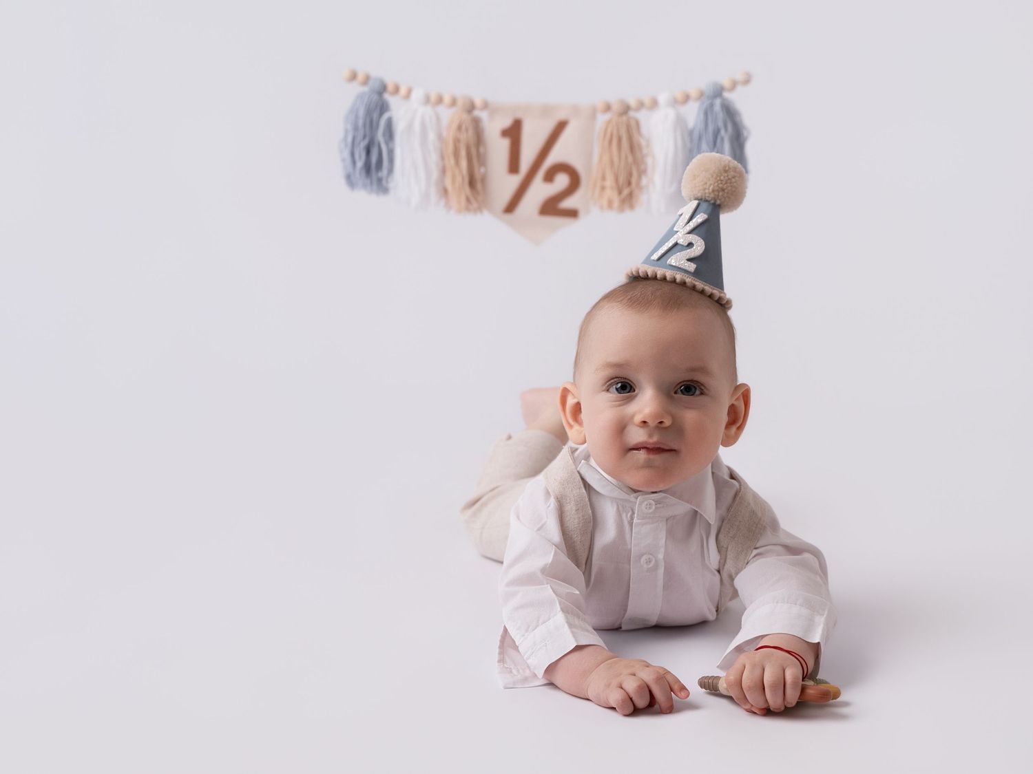 Adorable baby in a party hat celebrates their half birthday milestone with a decorative 1/2 banner backdrop.