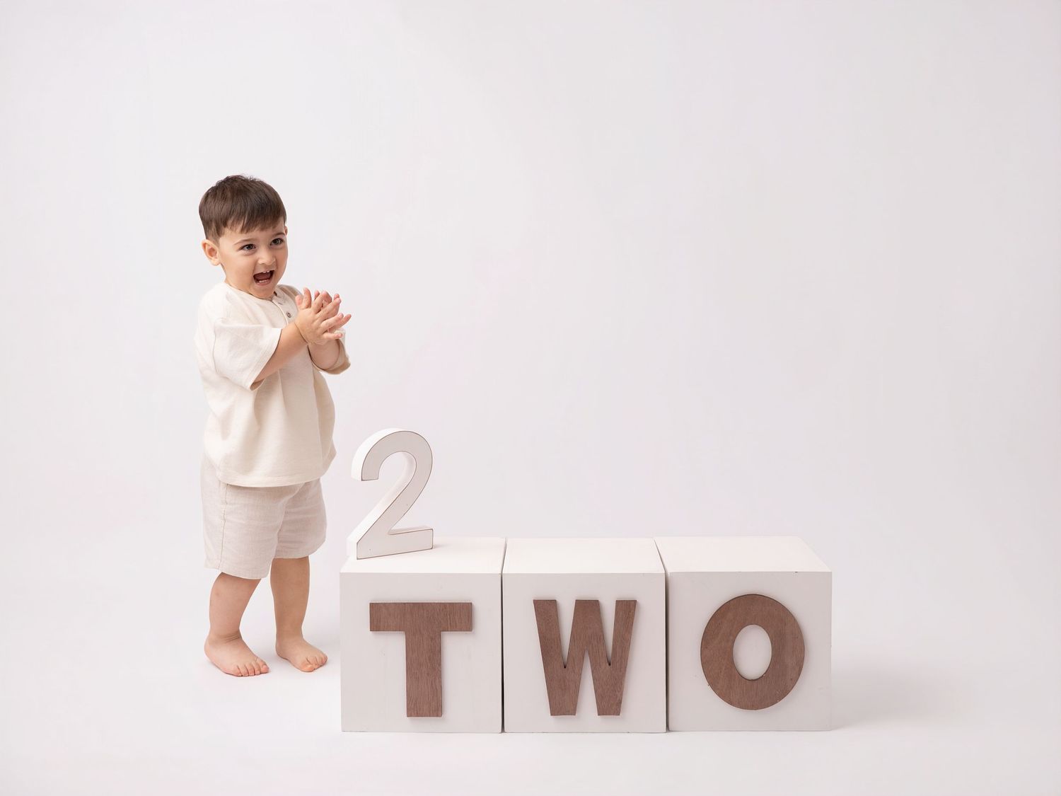Toddler standing next to large wooden blocks spelling TWO for a second birthday photo session.