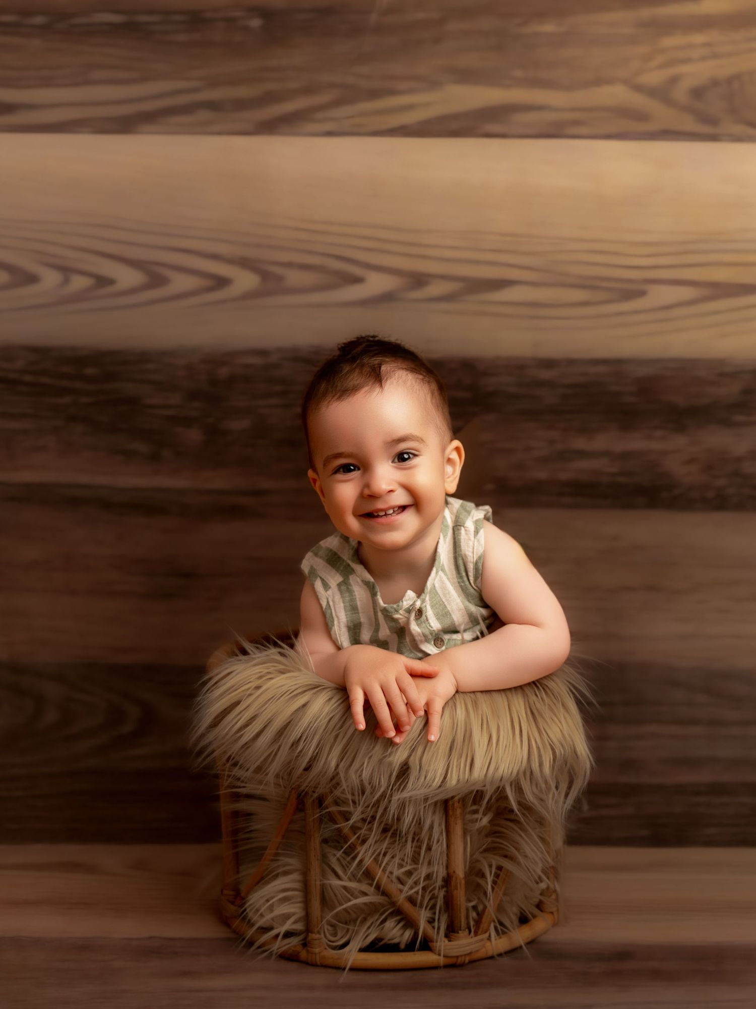 Smiling baby sitting in a rustic wicker basket with fluffy fur lining against a wooden plank backdrop.